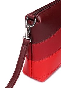 Červená a burgundská kožená crossbody taška se zipovým uzávěrem, odnímatelným popruhem a viditelnými švy na povrchu.
