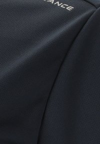 Close-up af mørkeblå tekstureret stof med små perforeringer og delvis hvid tekst trykt på.