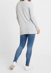 Szary sweter z długim rękawem z dzianiny z bocznymi rozcięciami, zestawiony z niebieskimi obcisłymi dżinsami i białymi trampkami. Gładka faktura i luźny krój.