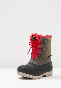 Wodoodporne buty za kolano z czarną gumową podeszwą, zielonym materiałem wierzchnim, czerwonym sznurkiem na górze i szarymi teksturowanymi akcentami na podeszwie.