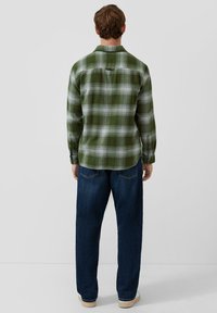 Zielona flanelowa koszula w kratę z mankietami na guziki, prostym krojem i detalem karczka z tyłu, noszona z ciemnymi jeansami i jasnymi butami.