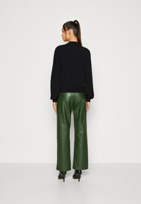 Black knitted sweater with long, voluminous sleeves, paired with high-waisted, wide-leg green leather pants and black heeled boots.