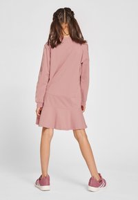 Rosa langärmliges Kleid mit ausgestelltem Saum und elastischen Bündchen, kombiniert mit rosa Sportschuhen mit weißen Akzenten. Schlichtes Design, ohne Muster.