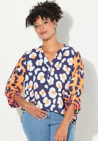 Blusa colorata realizzata in tessuto leggero, con sfondo color navy e motivi astratti arancioni, bianchi e neri; maniche 3/4 e dettagli con bottoni.