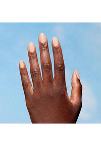 Mano di colore scuro con unghie a mandorla ben curate di un beige chiaro, mostrata su uno sfondo blu. Pelle liscia.