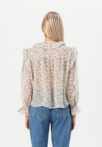 Blouse florale légère en tissu transparent, dotée d'un col et de poignets volants, avec une coupe ample et des motifs délicats dans des teintes douces. Associée à un denim.