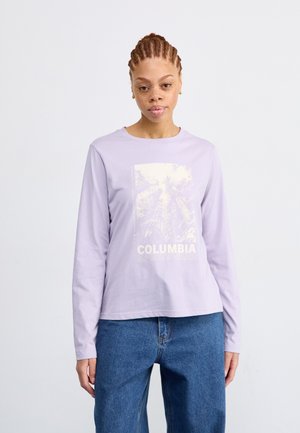Langærmet lavendelfarvet t-shirt med grafisk tryk med "COLUMBIA" i hvid, parret med blå jeans. Blødt stof og afslappet pasform.