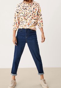Bluse mit floralem Multicolor-Muster, aus leichtem Stoff, runder Ausschnitt und 3/4-Ärmel, kombiniert mit dunkelblauen Jeans mit hochgekrempelten Säumen.
