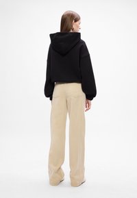 Felpa nera corta con cappuccio, abbinata a pantaloni ampi beige chiaro. Tessuto morbido, design semplice e senza motivi visibili.