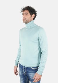 Maglione a collo alto azzurro chiaro in tessuto morbido con design aderente e scollo a coste, abbinato a jeans in denim strappati.