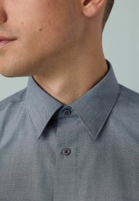 Graues Hemd mit Knopfleiste, strukturiertem Kragen, weichem Stoff und zwei Knöpfen sowie einem dezenten gewebten Muster.