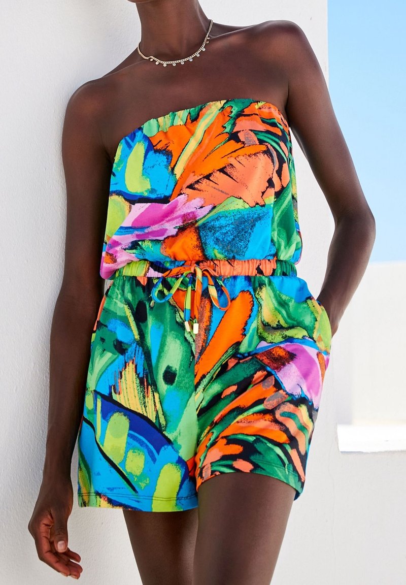 Combinaison sans manches multicolore avec des motifs abstraits vibrants dans des tons de vert, d'orange, de rose et de bleu. Ceinture élastique et poches latérales.