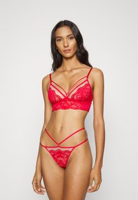 Conjunto de lingerie de renda vermelha com um bralette com alças ajustáveis e um thong combinado com tiras laterais finas e padrões florais.