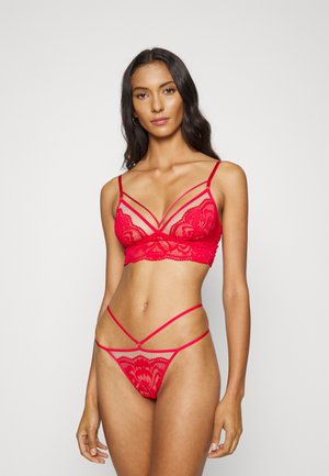 Conjunto de lingerie de renda vermelha com um bralette com alças ajustáveis e um thong combinado com tiras laterais finas e padrões florais.
