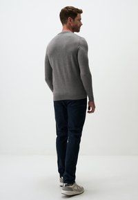 Pull gris à manches longues avec un col rond, ajusté. Associé à un pantalon bleu marine foncé et à des baskets gris clair. Design simple et minimaliste.