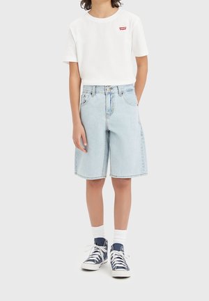 Barn iført hvid Levi's t-shirt, lyseblå denim knælange shorts, hvide sokker og marineblå høje sneakers mod en ensfarvet baggrund.