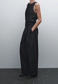 Musta hihaton yläosa, joka on valmistettu läpinäkyvästä kankaasta, yhdistetty korkeavyötäröisiin, leveisiin mustiin housuihin, joissa on pleateja ja sivupusseja. Litteät mustat kengät.