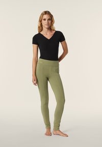 Bodysuit negro de manga corta combinado con leggings ajustados verde oliva que cuentan con una cinturilla alta y detalles de costura estructurada.