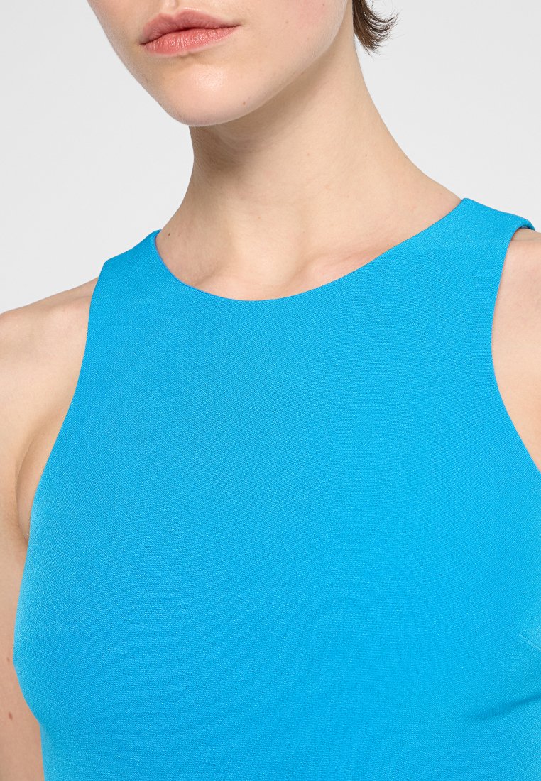 Close-up van een persoon in een mouwloos felblauw topje met een ronde halslijn, waarbij de nek, schouders en bovenste borst zichtbaar zijn.