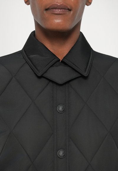Schwarze gesteppte Jacke mit hohem Kragen, die über einen Knopfverschluss und eine glatte Textur verfügt. Das Design umfasst durchgehende Rauten- Muster.
