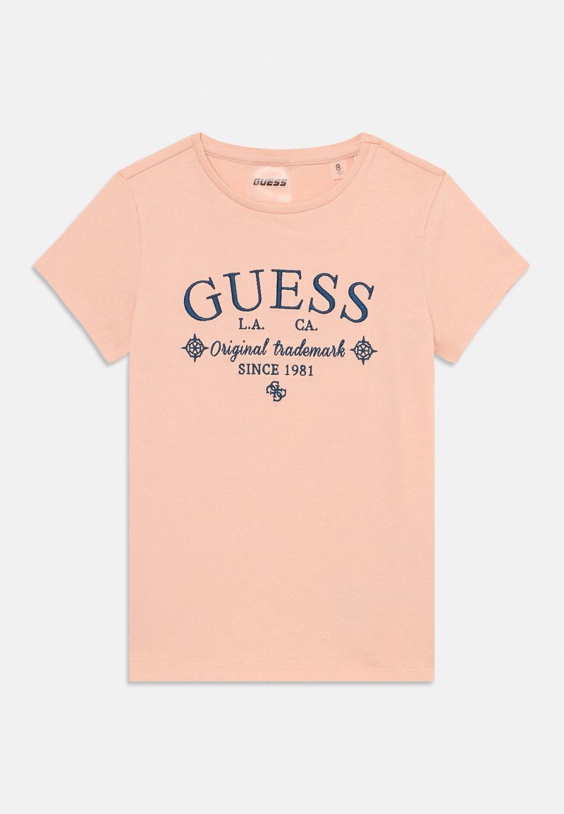 Šviesiai rožinė T-shirt marškinėliai su apvalia iškirpte ir trumpomis rankovėmis, su mėlynu "GUESS" logotipu ir dekoratyviniais elementais atspausdintais ant priekio.