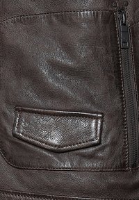 Ruskea nahkatakki, jossa on teksturoitu pinta. Siinä on suorakulmainen tasku, kontrastipistoja ja sivuvetoketju.