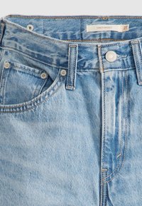 Jean en denim bleu clair avec passants visibles, fermeture par bouton, poche avant et étiquette indiquant "Cinch Baggy 27" à l'intérieur de la ceinture.