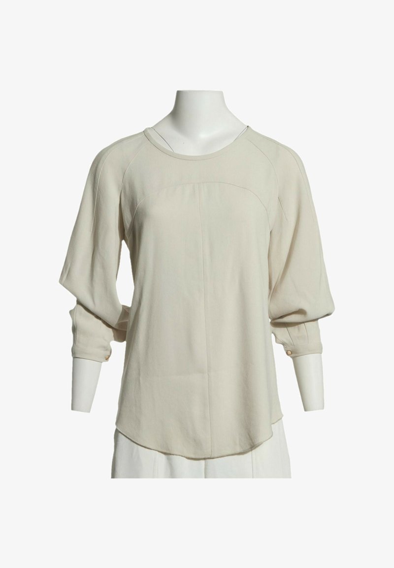 Blouse beige à manches longues avec col rond, coupe ample et poignets boutonnés, présentée sur un mannequin blanc sans tête.