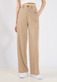 Beige op maat gemaakte broek met een hoge taille, wijde pijpen, steekzakken en een knoopsluiting, gemaakt van een gladde, lichte stof.