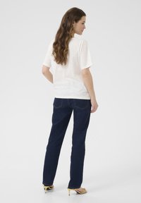 T-shirt en coton blanc à manches courtes, associé à un jean en denim bleu foncé et des sandales à talons jaunes, vu de dos.