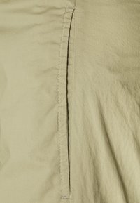 Licht kaki stof met een zachte textuur heeft een verticale splitdetail, omlijnd door contrasterende stiksels. Het minimalistische ontwerp richt zich op eenvoud.