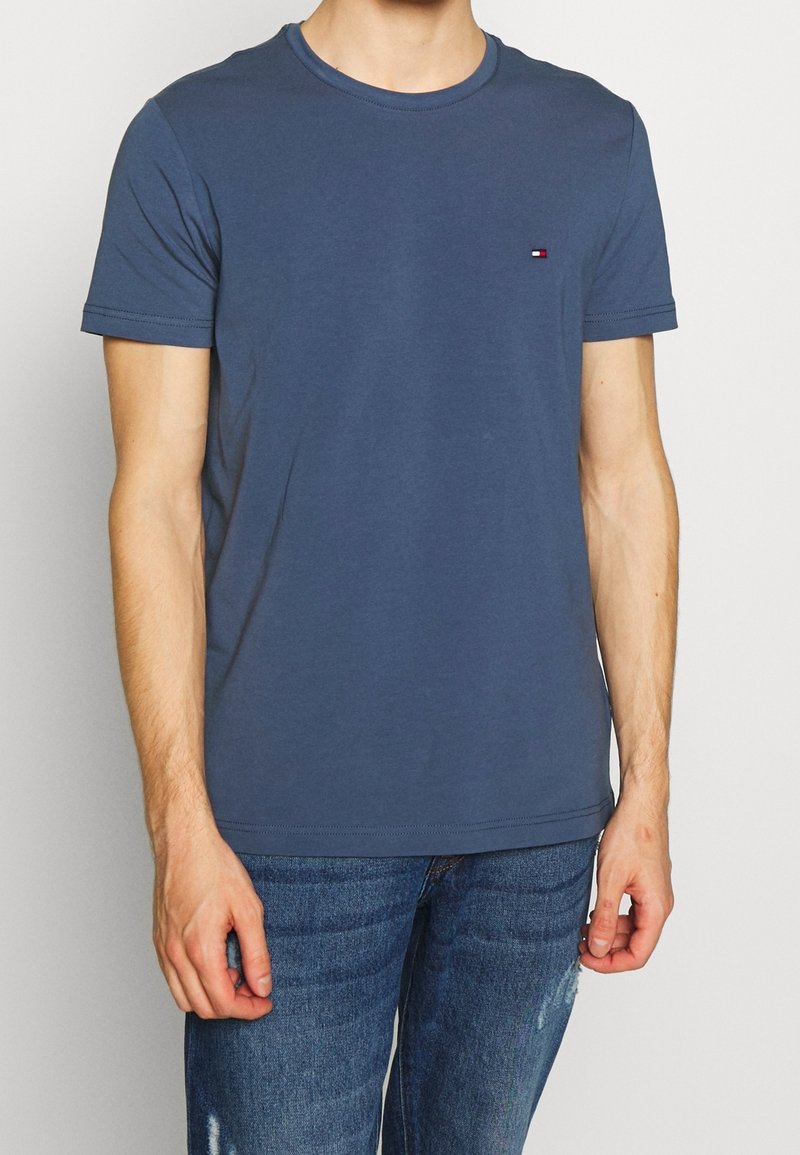Camiseta de algodón azul con mangas cortas, escote redondo y un pequeño logo en el lado izquierdo del pecho. Textura suave y ajuste casual.