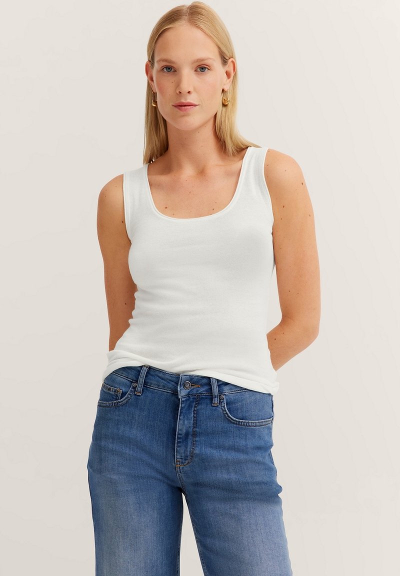 Weißes ärmelloses Tanktop mit Rundhalsausschnitt, kombiniert mit blauen Jeans aus Denim, die einen dezenten Farbverlauf und ein klassisches Fünf-Taschen-Design aufweisen.