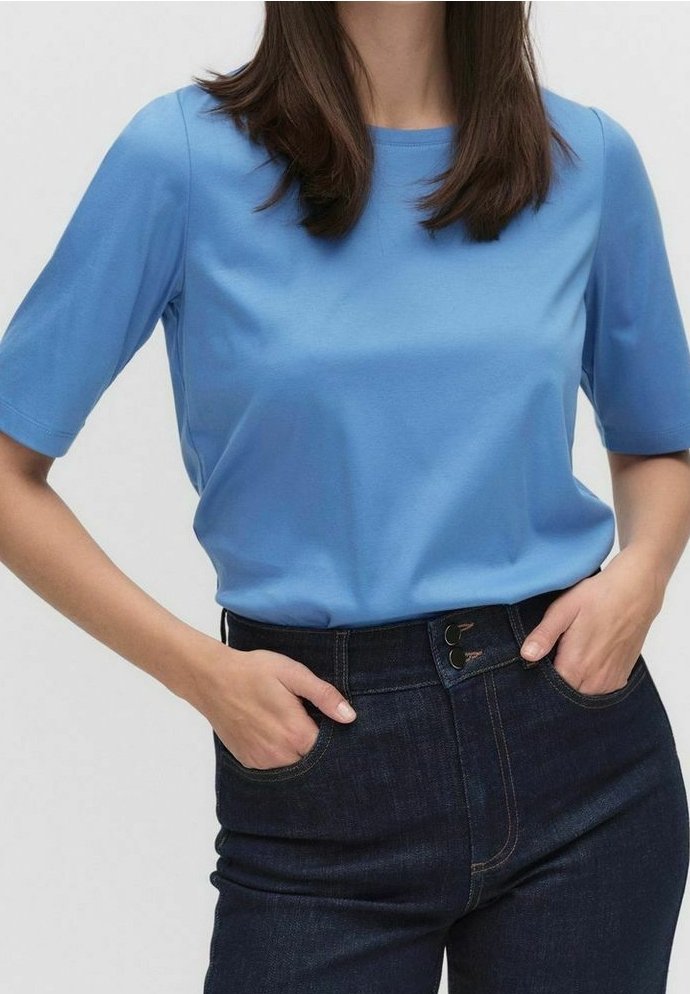 Světle modré tričko z měkké látky, s krátkými rukávy a kulatým výstřihem, v kombinaci s tmavě modrými džíny s vysokým pasem a zapínáním na knoflík.