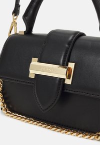 Svart läderhandväska med gul metallspänne graverad "ALDO", kort handtag och guldkedjedetalj vid basen.