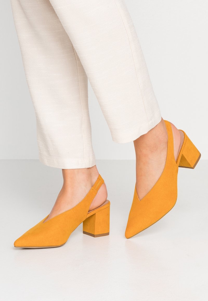 Chaussures slingback en daim jaune avec un bout pointu et un talon carré, associées à un pantalon cropped beige clair.
