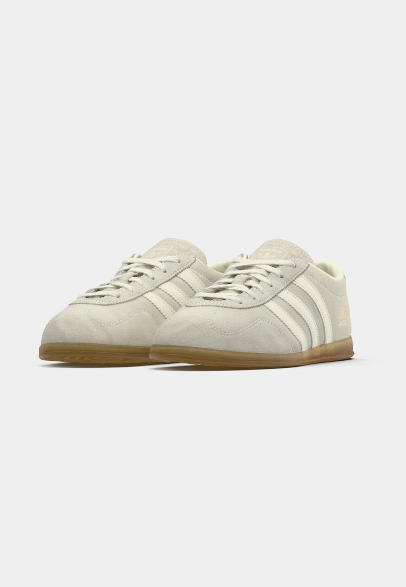 Light grey suede sneakers with white striped accents, lace-up closure, and gum rubber sole. Features a textured surface and minimal branding.