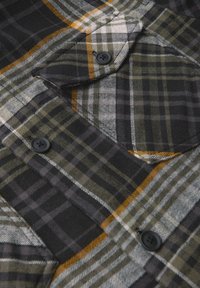 Camicia a quadri nei colori nero, grigio, verde e arancione. Realizzata in tessuto morbido, presenta bottoni neri e due tasche sul petto.