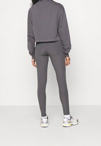 Szara, skrócona bluza z długimi rękawami i luźnym krojem, w zestawieniu ze szarymi legginsami. Model nosi białe i srebrne buty sportowe.