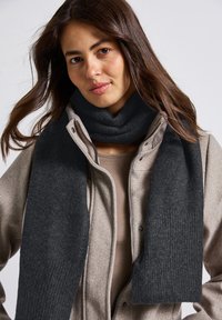 Mørkegrå uldsjal med en ribbet tekstur, viklet omkring en beige zip-up frakke, der fremhæver dens varme og bløde stof.