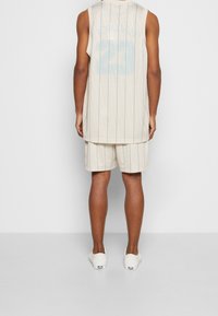 Beige nätlinne med vertikala blåränder och "JORDAN 23" på baksidan, kombinerat med matchande beige shorts och lätta sneakers.