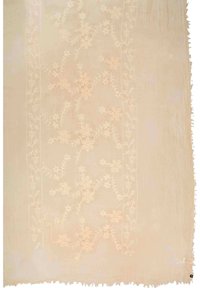 Broderat tyg med en mjuk beige bakgrund, med blommönster i ljusare nyanser och en fransad kant. Texturerad yta synlig.