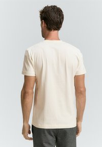Tricou scurt cu mânecă, de culoare crem, realizat din bumbac, având un guler rotund și o textură fină, prezentat din spate.