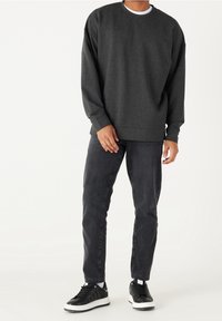 Sudadera gris oscuro de manga larga y escote redondo, combinada con jeans negros y zapatillas negras con suelas blancas.