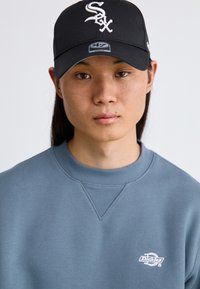 Cappellino da baseball nero con logo bianco, felpa grigia con colletto a coste e piccolo logo sul petto. Tessuto morbido e design semplice.