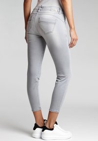 Jeans skinny gris claro con una textura suave, cinco bolsillos y pierna cónica, combinados con zapatillas blancas con detalles en negro.