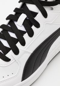 Baskets blanches avec des accents noirs, panneaux en cuir texturé, lacets plats noirs et perforations. Présente une finition lisse et un col rembourré.