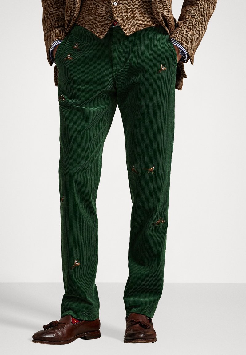 Green corduroy pants featuring decorative embroidered birds, straight cut, and subtle ribbed texture. Paired with brown shoes.