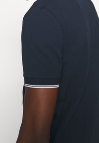 Mörkblå polo med en texturerad tyg. Korta ärmar har vita randiga detaljer vid manschetterna. Skräddarsydd passform med en diskret krage.