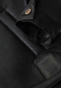 Black leather jacket with a smooth texture, featuring a visible button closure and a rectangular logo patch on the left side.